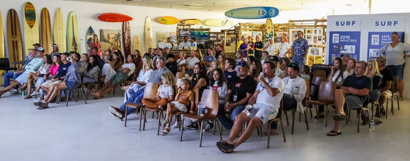 A packed audience of all ages seated among the museum's surfboards for a program in the gallery